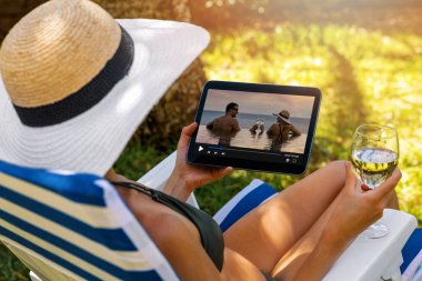 Kadın bahçe sandalyesinde dinlenirken medya yayını üzerine romantik bir film izliyor.