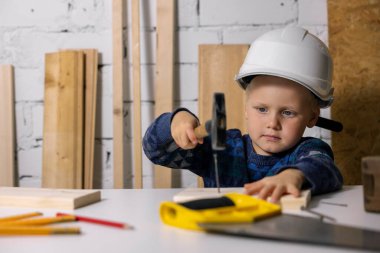 Kasklı küçük çocuk marangoz atölyesinde tahta çivi çakmayı öğrendi.