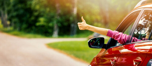woman inside car on the road trip with thumb up gesture out of the window. banner with copy space