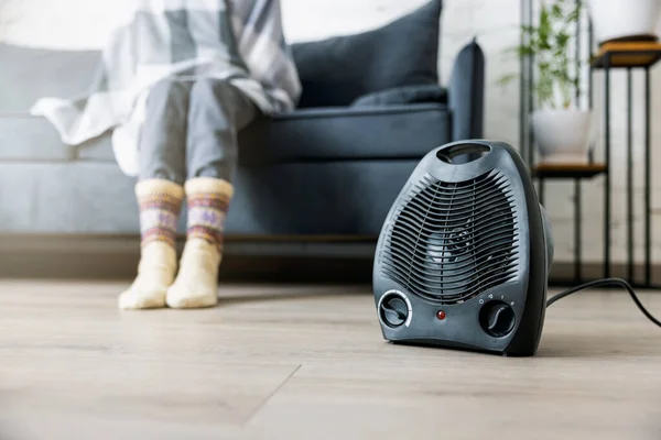 woman warming cold room with electric heater at home. heating season