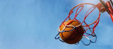 Basketbol topu açık hava sokak sahasında mavi gökyüzü arka planına karşı puan topluyor. Kopyalama alanı olan pankart