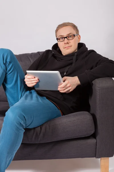 A man lying on a sofa and has a tablet PC in his hands — Stock Photo, Image