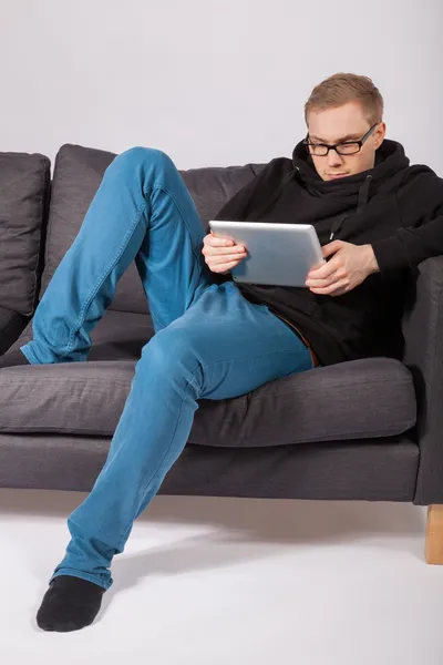 Мужчина лежит на диване и держит в руках планшетный компьютер — стоковое фото
