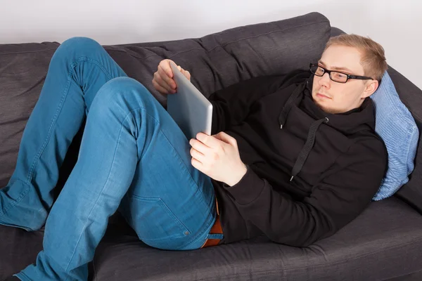 A 남자는 소파에 누워 있으며 그의 손에 태블릿 Pc — 스톡 사진