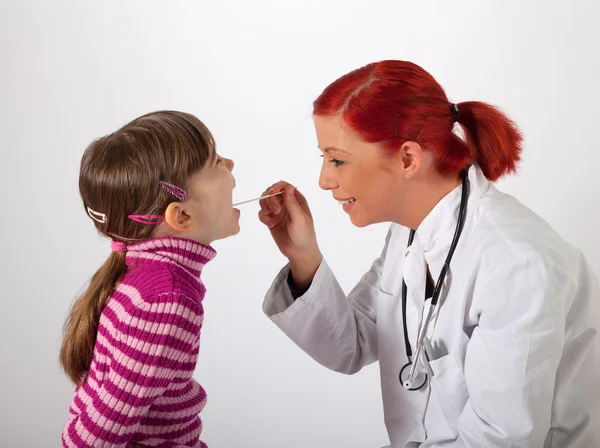 Ο παιδίατρος κοιτάζει ένα κοριτσάκι στο στόμα Εικόνα Αρχείου