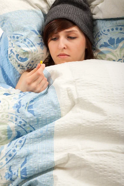 Het jonge meisje ligt ziek in bed en haar geneesmiddel inneemt — Stockfoto