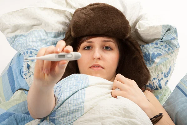 La joven está acostada enferma en la cama y tomando su temperatura —  Fotos de Stock