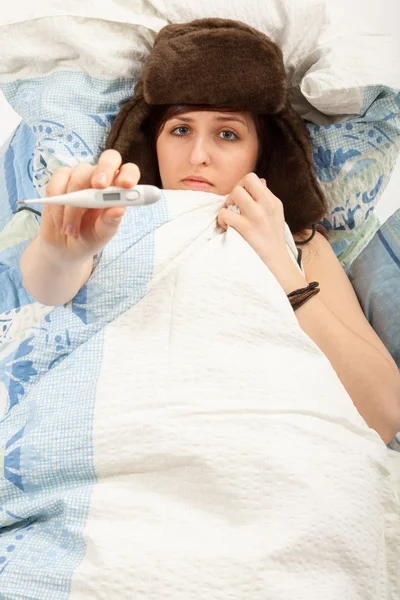 La joven está acostada enferma en la cama y tomando su temperatura —  Fotos de Stock