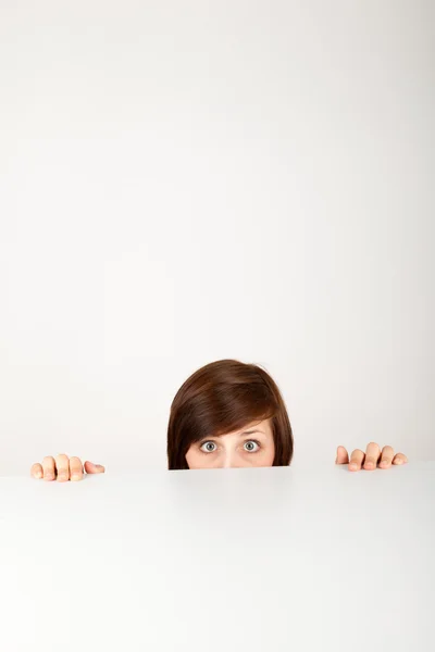 The young woman is hiding anxious behind the table — Stock Photo, Image