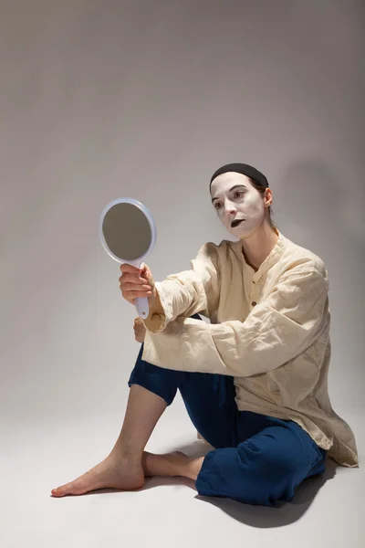 The clown is sitting on the ground with a mirror in his hand — Stock Photo, Image