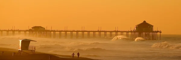 Şafakta huntington Beach plaj boyunca iki sörfçü yürümek.