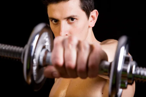 Молодой мускулистый человек поднимает тяжести на черном фоне — стоковое фото