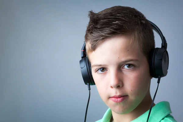 Portrait of a boy listening to music on headphones over grey bac — Stock Photo, Image