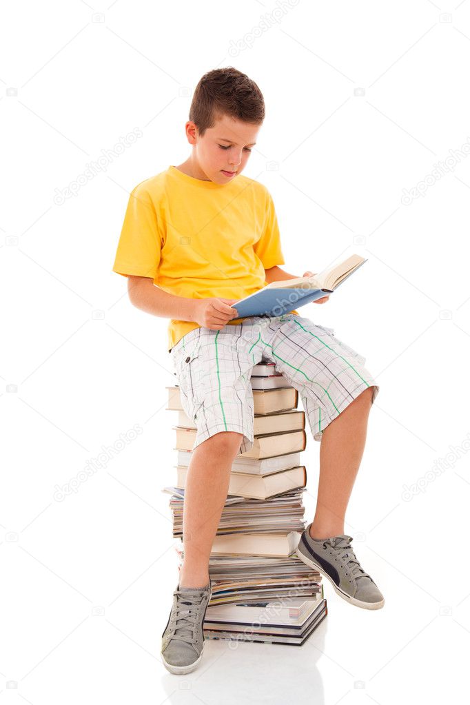 Young boy sitting on a pile of books reading against a white bac