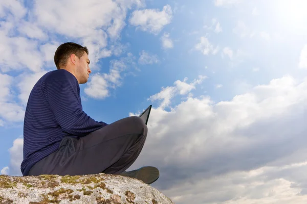 Jeune homme avec ordinateur portable à genoux au sommet d'une montagne — Photo