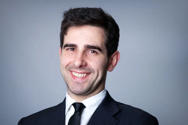 Close-up portrait of a smiling young business man on grey background — Stock Photo, Image