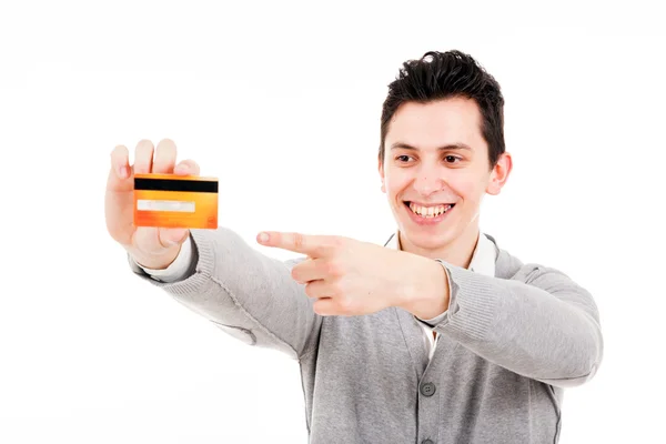 Feliz joven sonriente sosteniendo una tarjeta de crédito y señalando aislado sobre fondo blanco — Foto de Stock