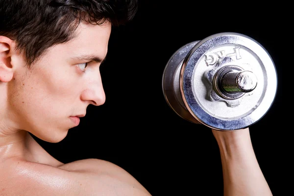 Junger muskulöser Mann stemmt Gewichte auf schwarzem Hintergrund — Stockfoto