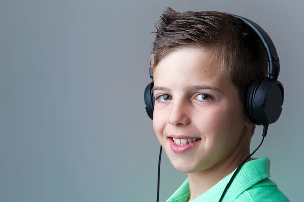 Portrait of a smiling boy listening to music on headphones over — Stock Photo, Image