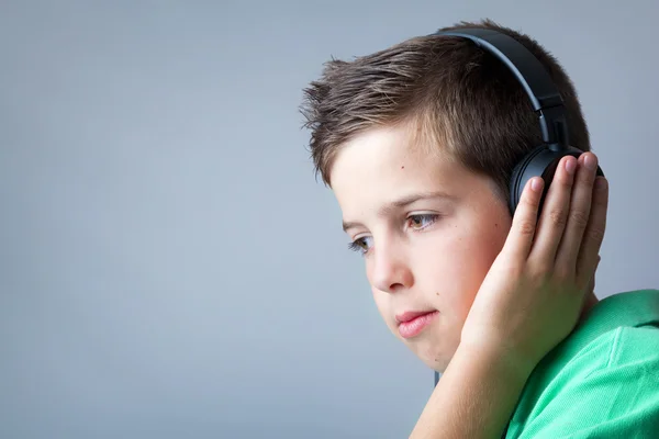 Portrait of a cute boy listening to music on headphones over gre — Stock Photo, Image