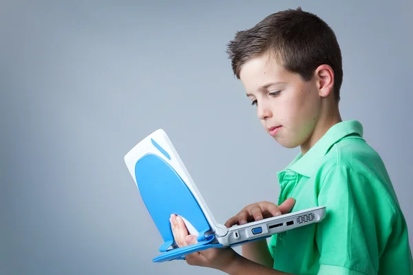 Jovem menino casual usando um laptop contra fundo cinza — Fotografia de Stock