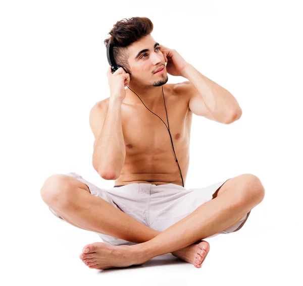 Shirtless young man sitting on the floor listening to music, isolated on white — Stock Photo, Image