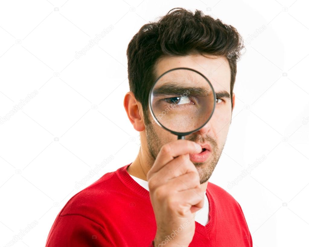 Curious young man looking through magnifying glass, isolated on white