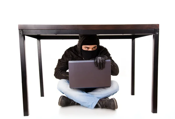 Un hacker con laptop nascosto sotto il tavolo dell'ufficio, isolato su bianco — Foto Stock