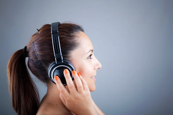 Menina bonita com fones de ouvido no fundo cinza — Fotografia de Stock