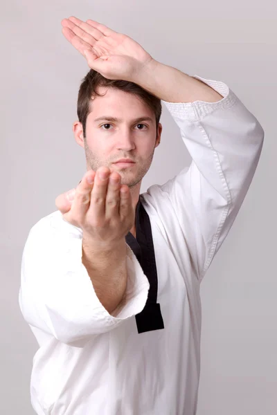 Jovem praticando artes marciais sobre fundo cinza — Fotografia de Stock