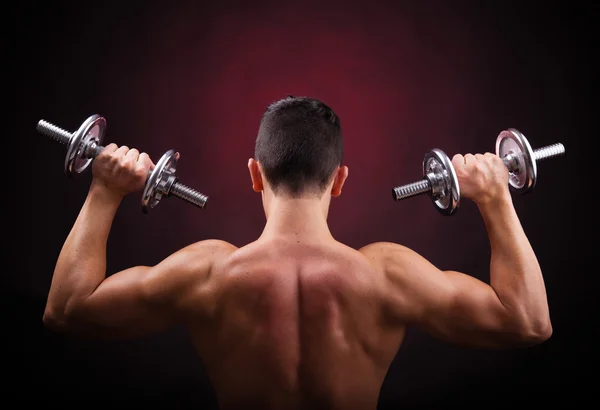 Muskulöser junger Mann stemmt Gewichte vor schwarzem Hintergrund — Stockfoto