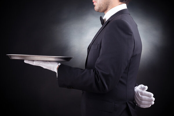 Обрезанное изображение молодого официанта, держащего пустое блюдо на черном "Б"
