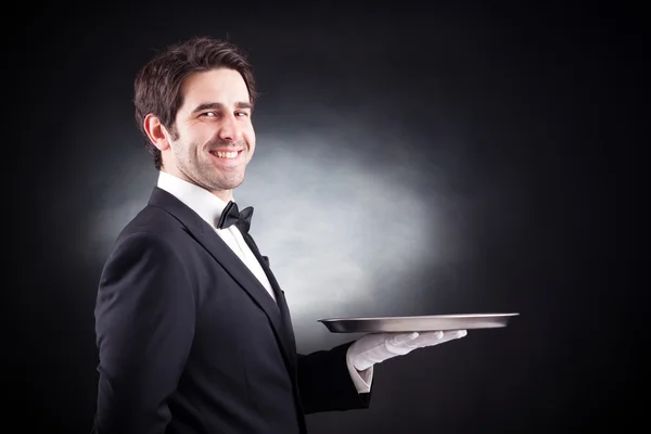 Портрет молодого офіціанта, який тримає порожню тарілку на чорному фоні — стокове фото