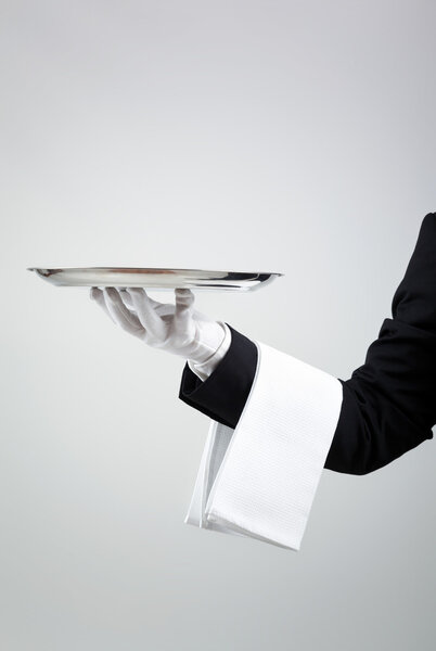 Официант держит пустой серебряный поднос на сером фоне

