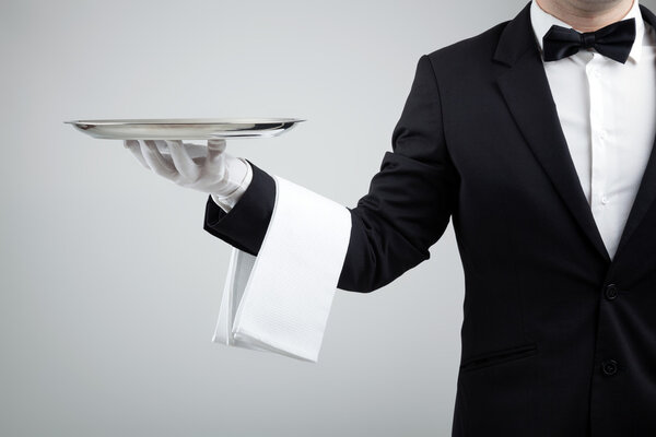 Waiter holding empty silver tray over gray background