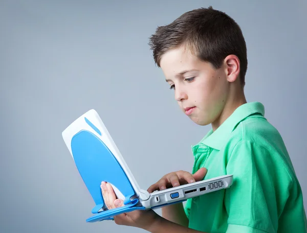 Jovem menino casual usando um laptop contra fundo cinza — Fotografia de Stock