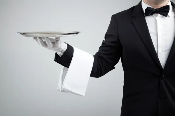 Číšník drží prázdný stříbrným podnosem nad šedým pozadím Stock Fotografie