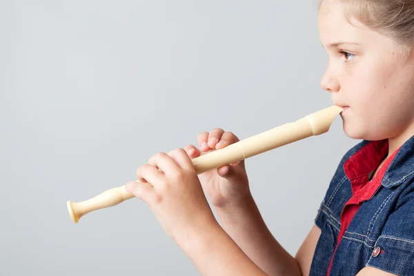 Imagen de una colegiala tocando la flauta sobre un fondo gris —  Fotos de Stock