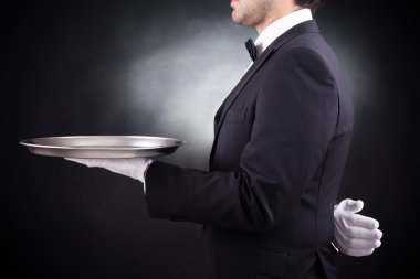 siyah arka plan üzerinde boş gümüş tepsi tutarak garson