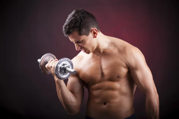 Muscular homem jovem levantando pesos no fundo escuro — Fotografia de Stock