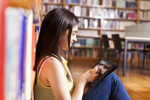 Fiatal női hallgató használ egy tabletta számítógép, egy könyvtárban — Stock Fotó