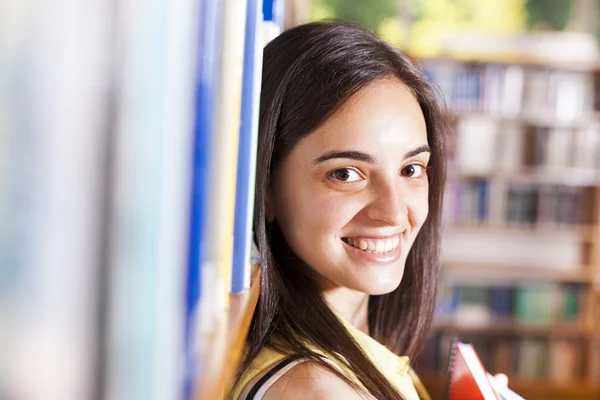 Portrait of pretty girl leaning on the bookshelves of library — Stock Photo, Image