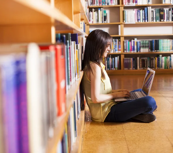 Fiatal mosolygó diák használ a laptop egy könyvtárban — Stock Fotó