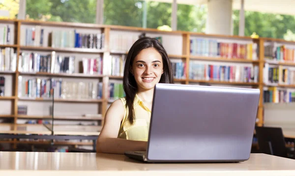 Sonriente estudiante que trabaja con portátil en una libr de la escuela secundaria — Foto de Stock
