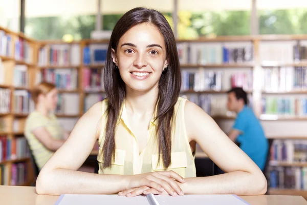 Sonriente chica mirando a la cámara en la biblioteca de la universidad con su colle —  Fotos de Stock