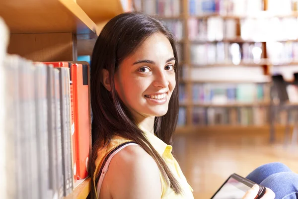 Estudante sorrindo usando um computador tablet em uma biblioteca universitária — Fotografia de Stock