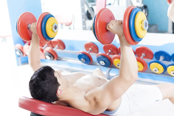 Shirtless young man lifting heavy free weights at the gym — Stock Photo, Image