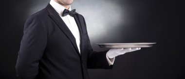 Waiter holding empty silver tray over black background clipart
