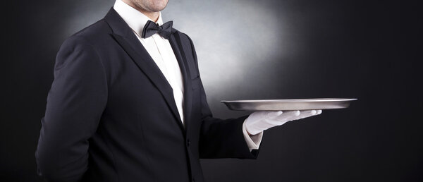 Waiter holding empty silver tray over black background