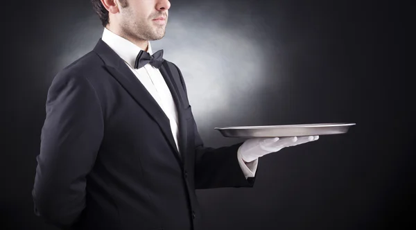 Waiter holding empty silver tray over black background — Stock Photo, Image